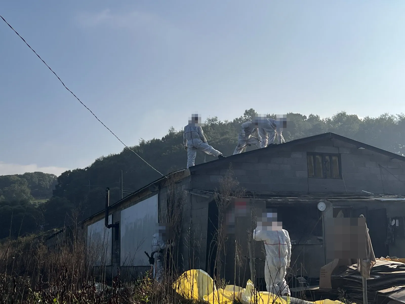 보호복 작업자들이 건물 지붕 위에서 지붕재를 해체한다