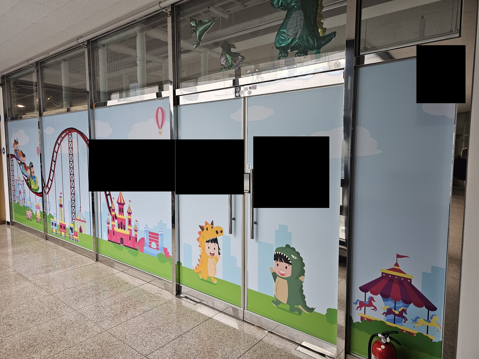 캐릭터 그래픽이 붙은 유리문과 유리 벽면이 보인다. 복도 바닥과 소화기가 보인다. 사진에 보이지 않는 범위나 과거 작업 이력은 확인하지 않았습니다.