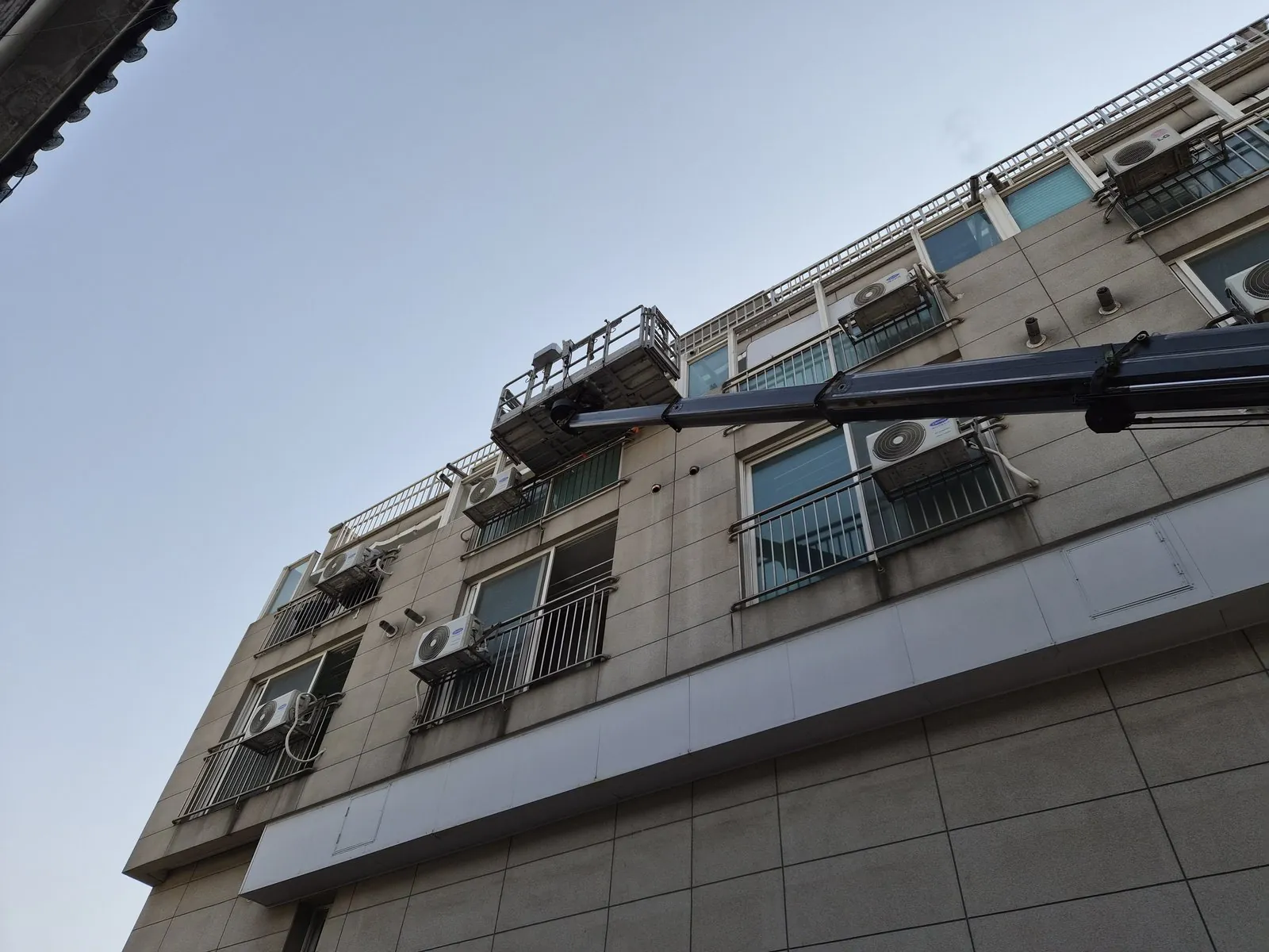 고소작업차 붐과 작업대가 건물 외벽 상층부에 접근해 있음