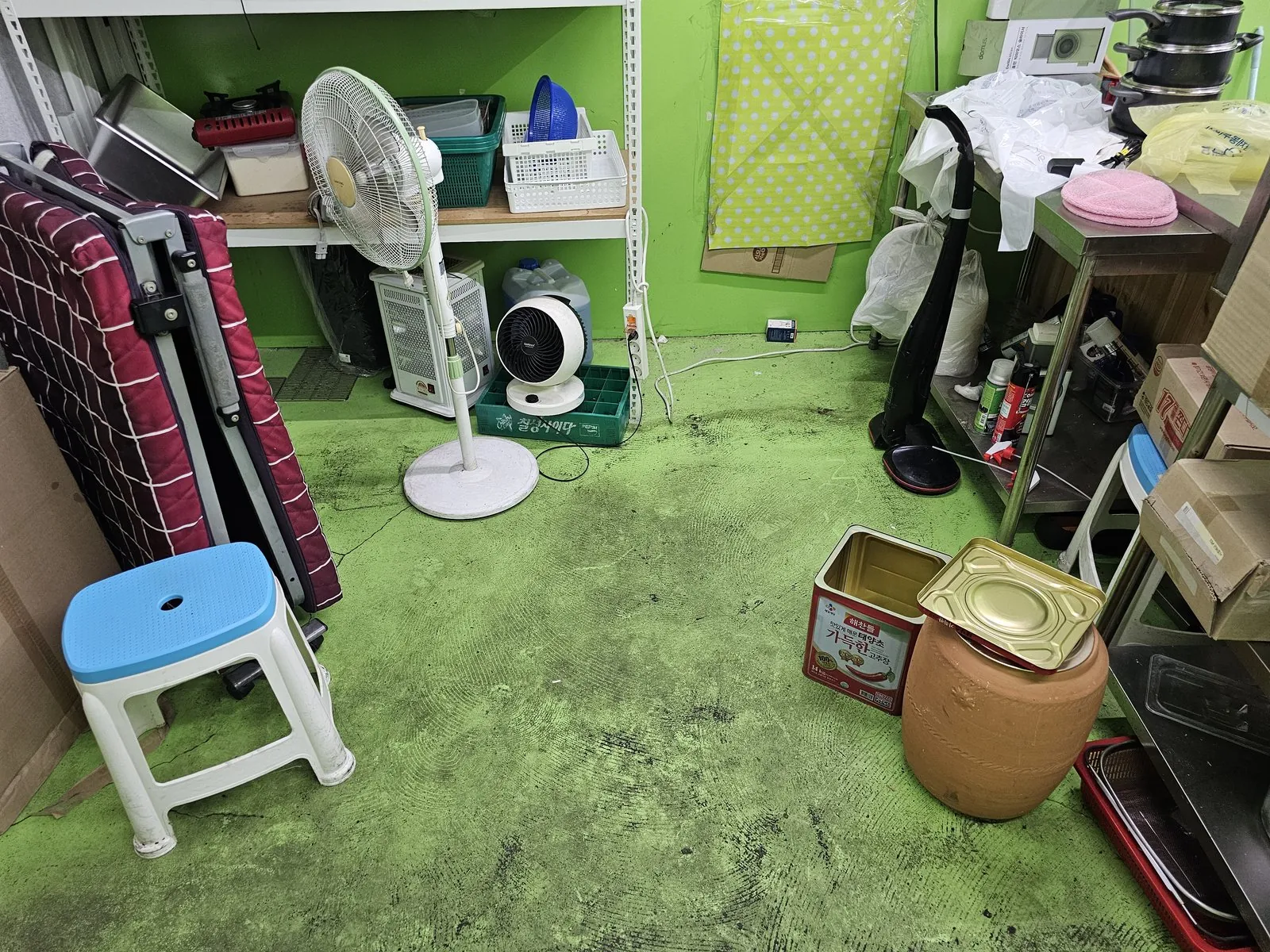 선풍기·접이식 침구 등 집기가 남은 초록 바닥 창고.