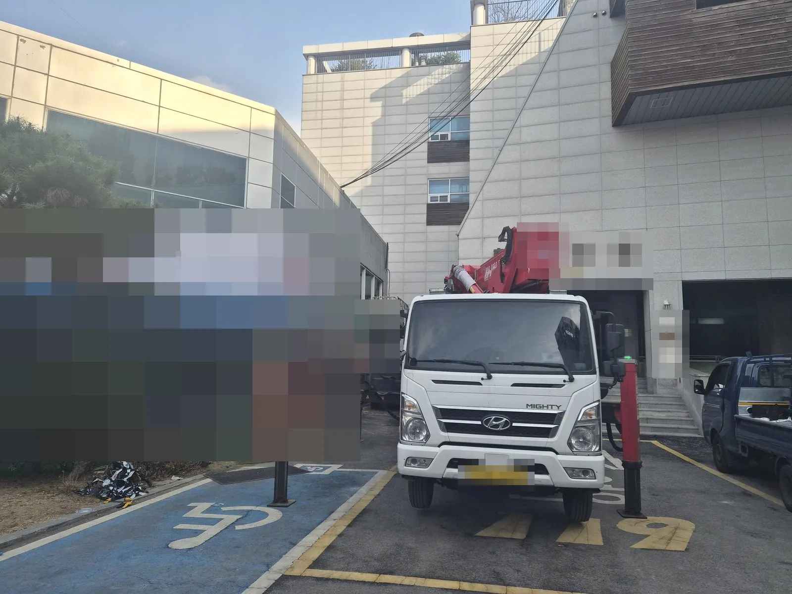 건물 앞 주차 구역에 고소작업차가 받침대를 내리고 서 있음