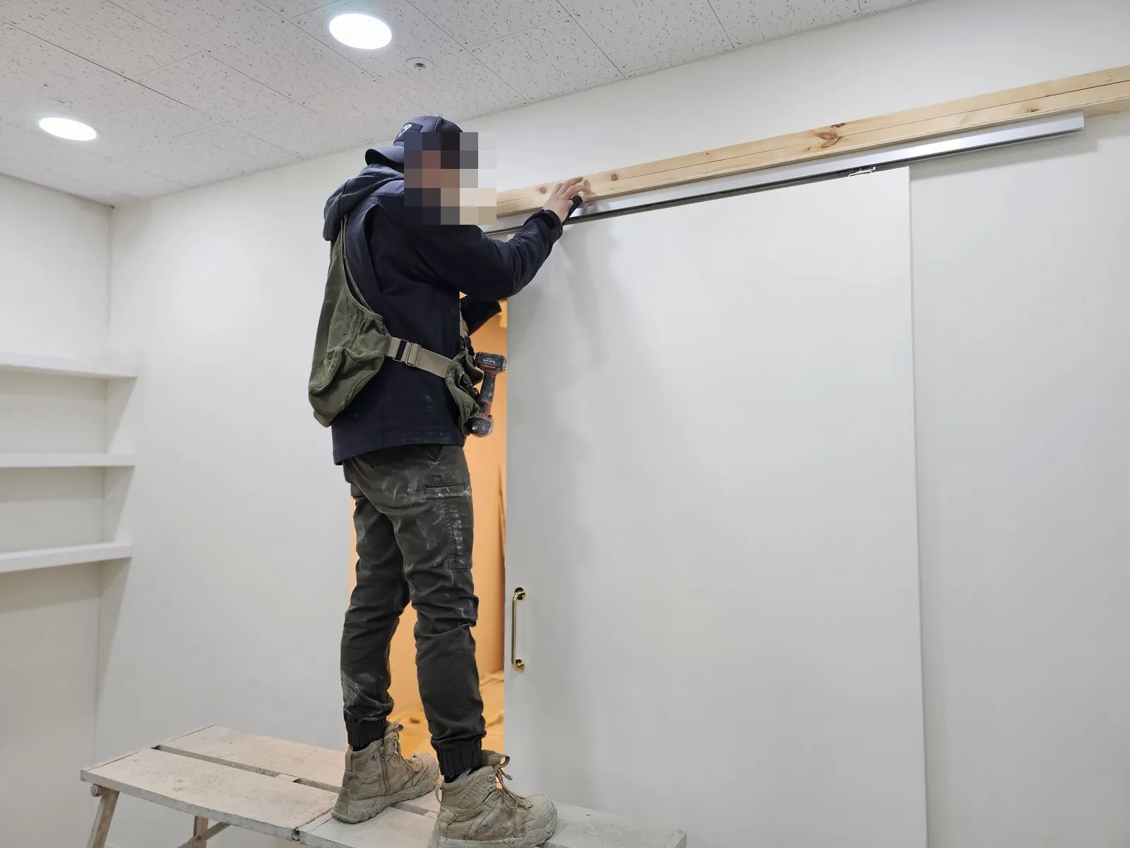 작업 발판 위에서 슬라이딩 도어 상부 레일 목재를 다루는 실내