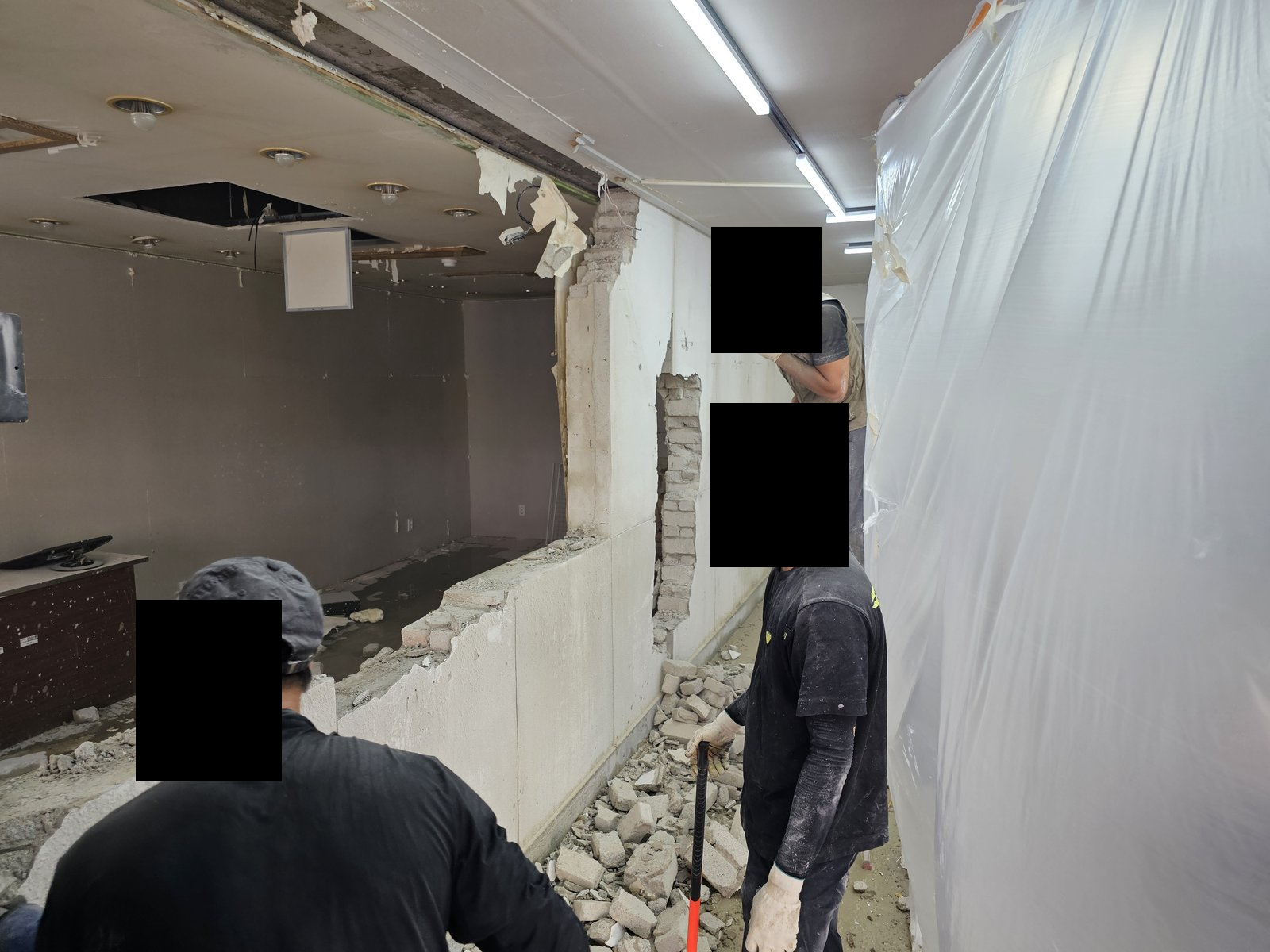 철거 중인 실내 벽체와 잔해, 비닐 가림막이 보인다. 작업자 세 명의 얼굴은 이미 검은 박스로 가려져 있다. 사진에 보이지 않는 범위나 과거 작업 이력은 확인하지 않았습니다.