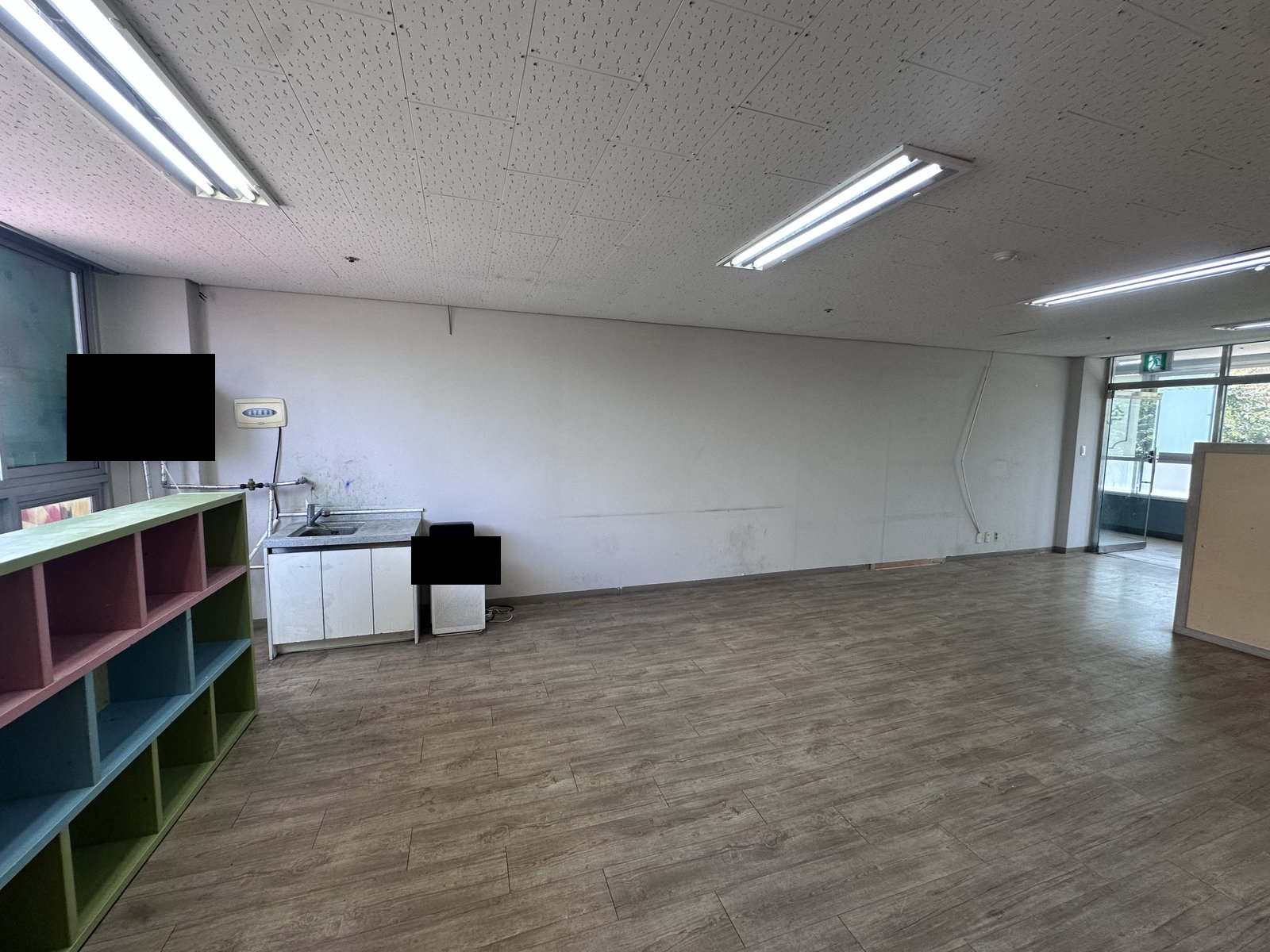 가구 외에 비어 있는 실내에 싱크대와 바닥재, 형광등이 보임. 일부 영역에 기존 검은 가림이 있음. 사진에 보이지 않는 범위나 과거 작업 이력은 확인하지 않았습니다.