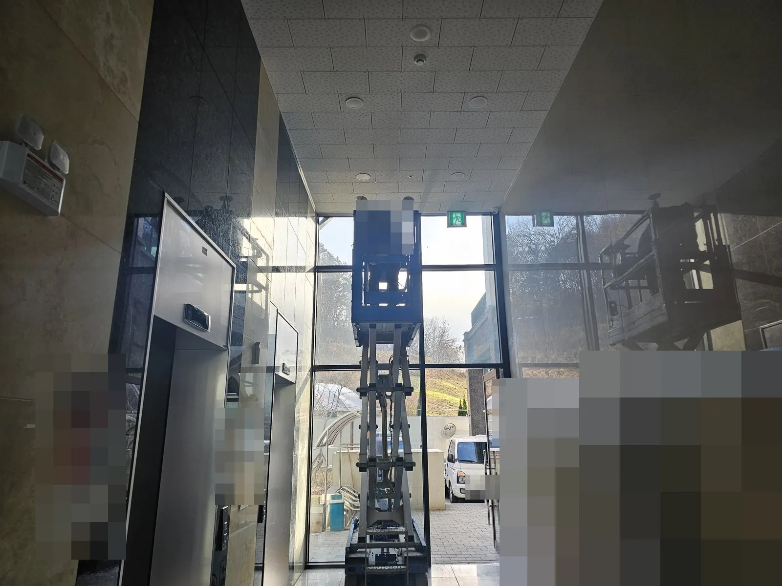 건물 로비 출입구에서 고소작업차로 천장 작업을 하는 모습