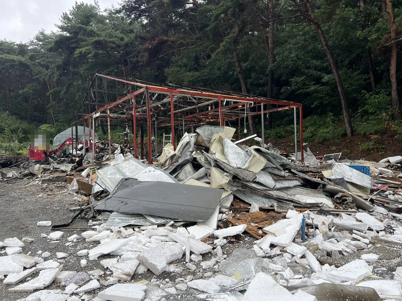 철골 골조 앞에 단열재와 철판 잔재가 쌓이고 굴착기가 정리 중