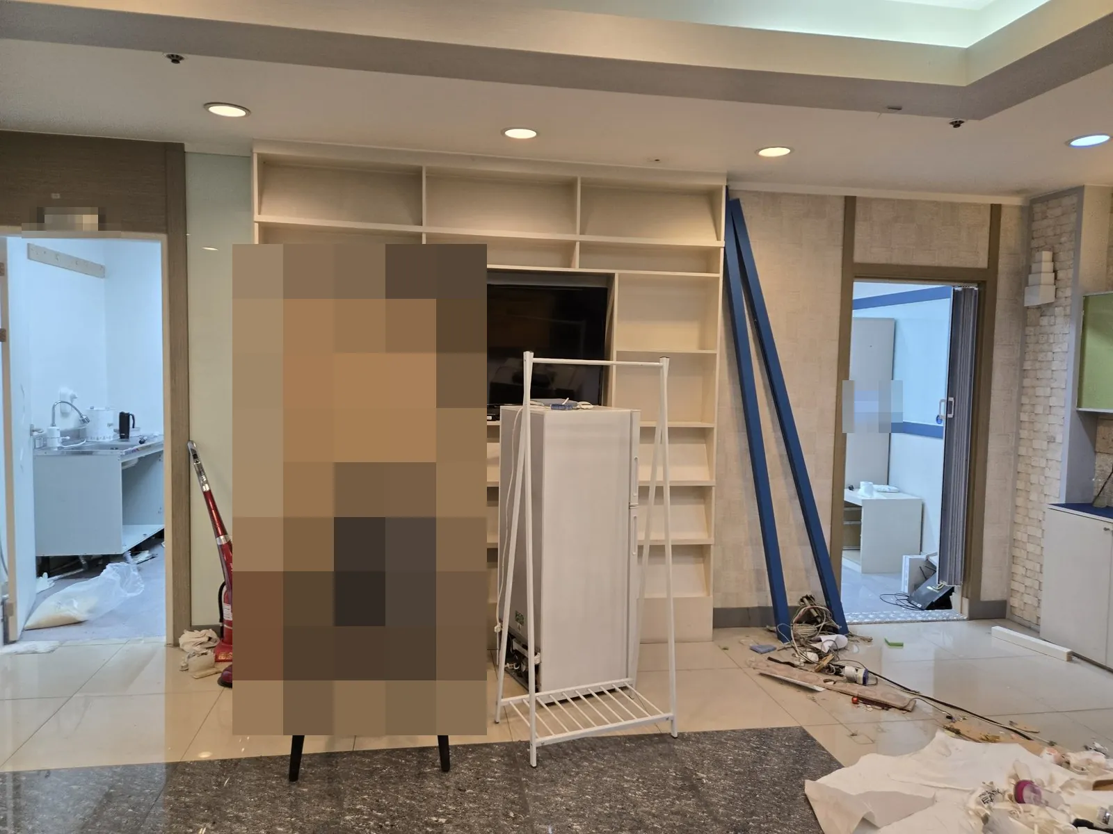 홀에 가구와 냉장고가 남아 있고 바닥에 전선과 잔재가 있다.