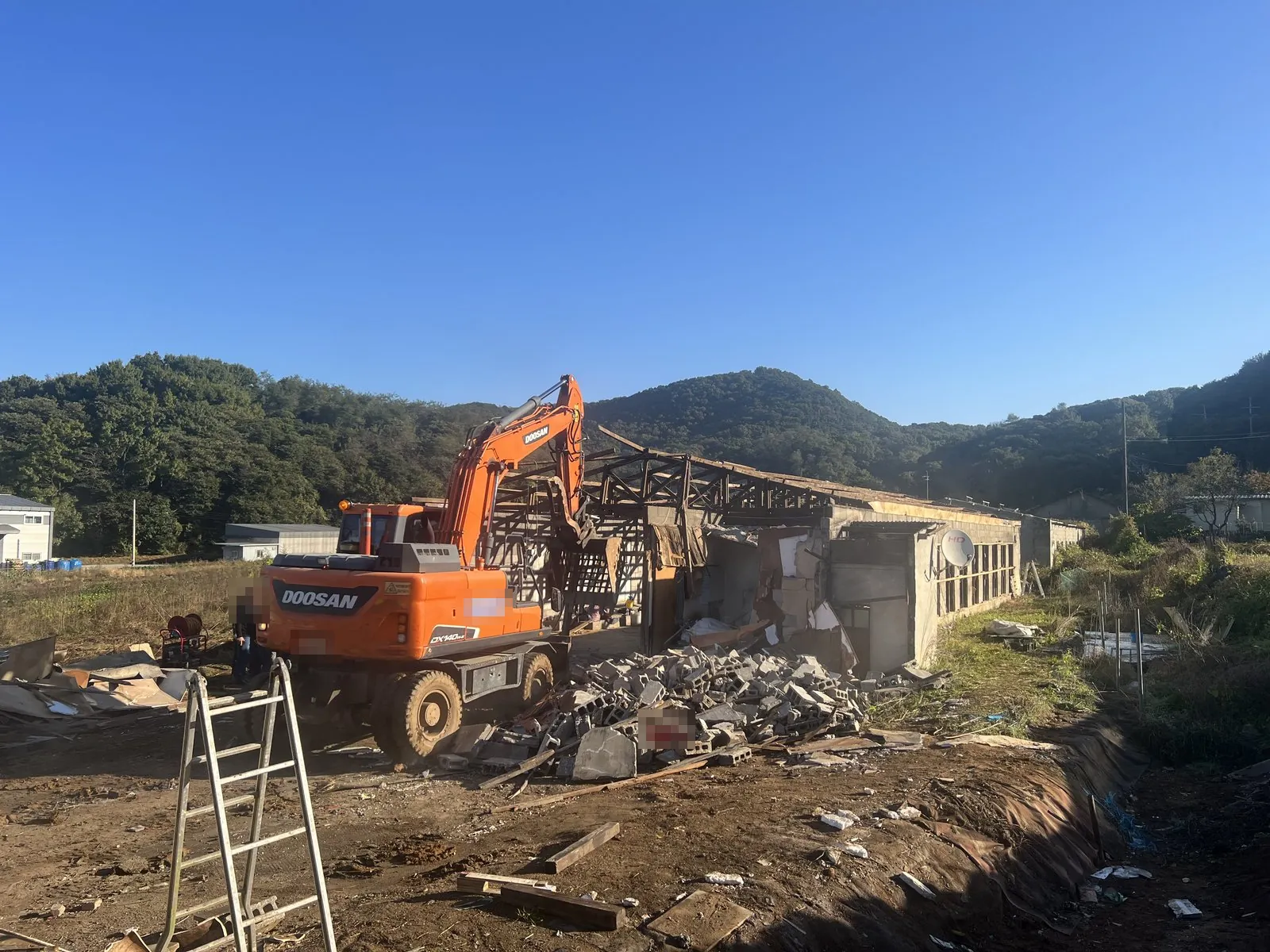 굴착기가 축사 건물을 해체하고 블록 잔해가 쌓여 있다